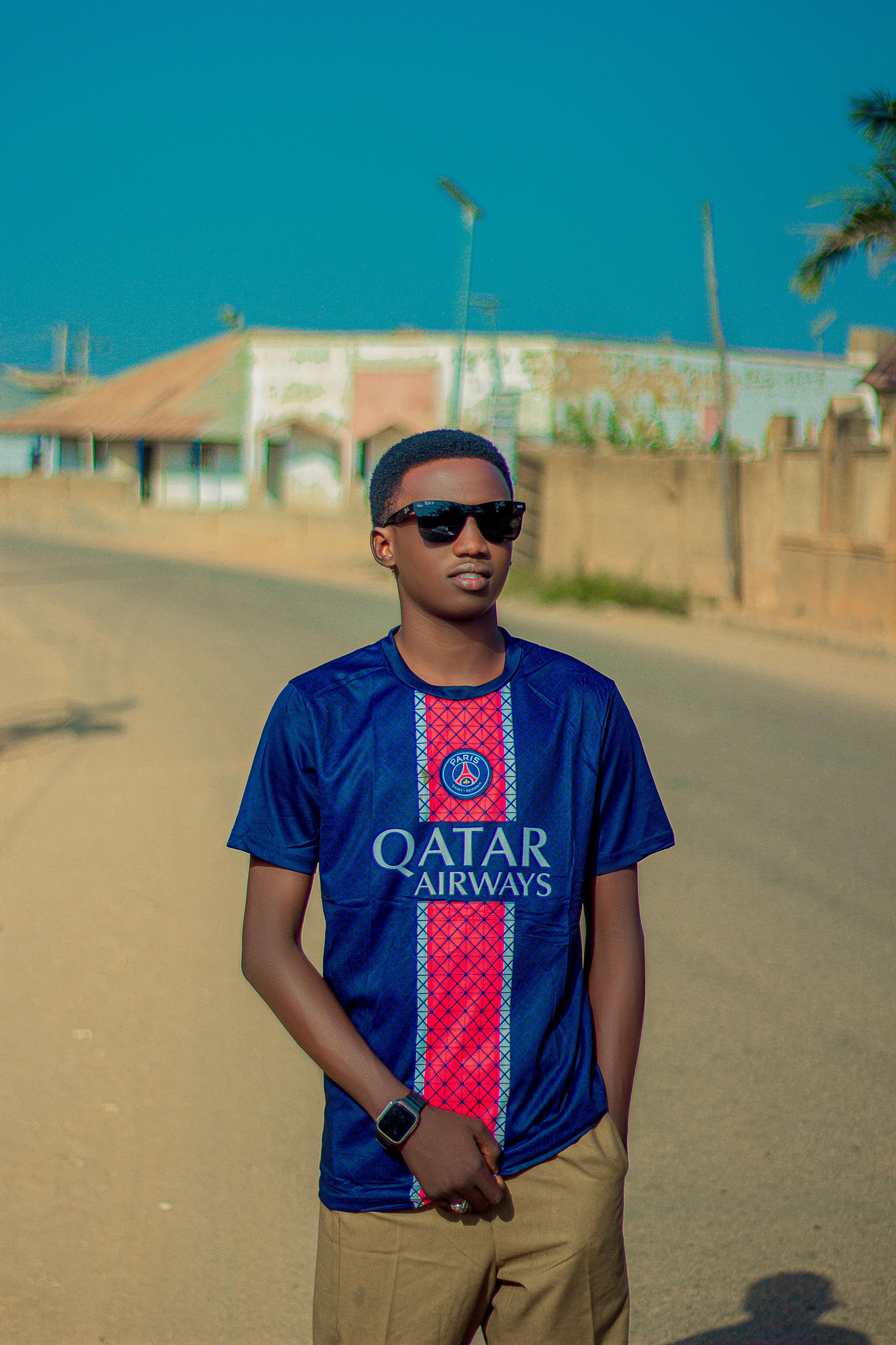 Stylish man in sunglasses and sports jersey standing confidently outdoors.