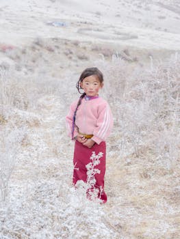 Child in bright attire stands in picturesque frosty field.