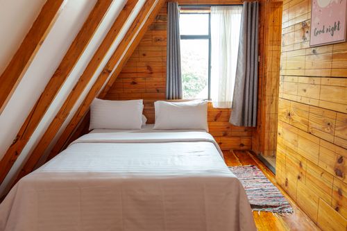 Free Warm and inviting A-frame cabin bedroom featuring wooden walls, white bedding, and natural light. Stock Photo