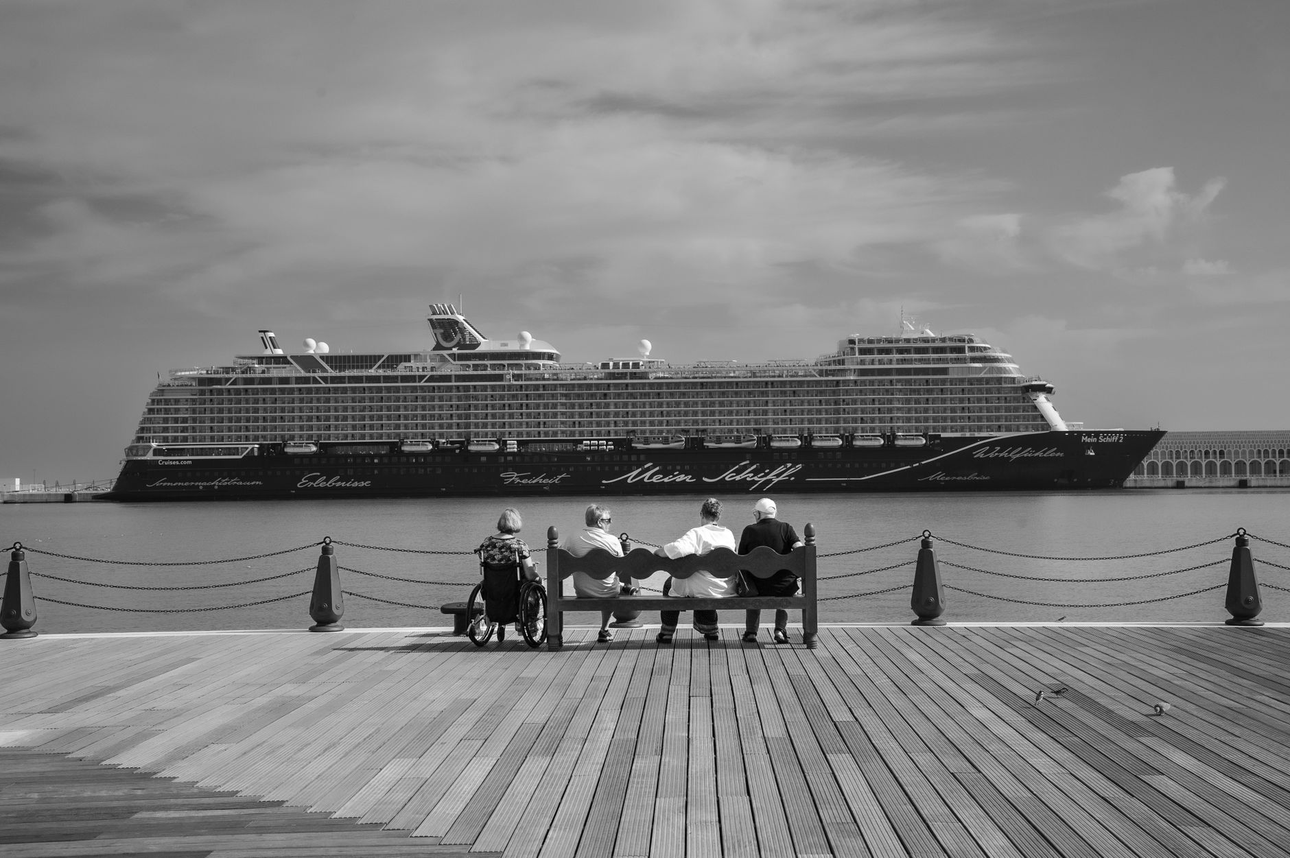 Monochrome view of a cruise ship with people seated on a pier front.