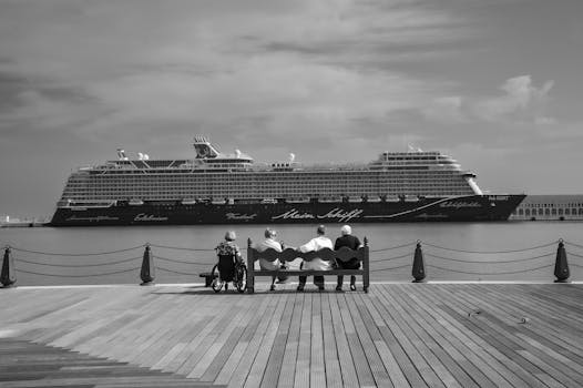 Monochrome view of a cruise ship with people seated on a pier front.