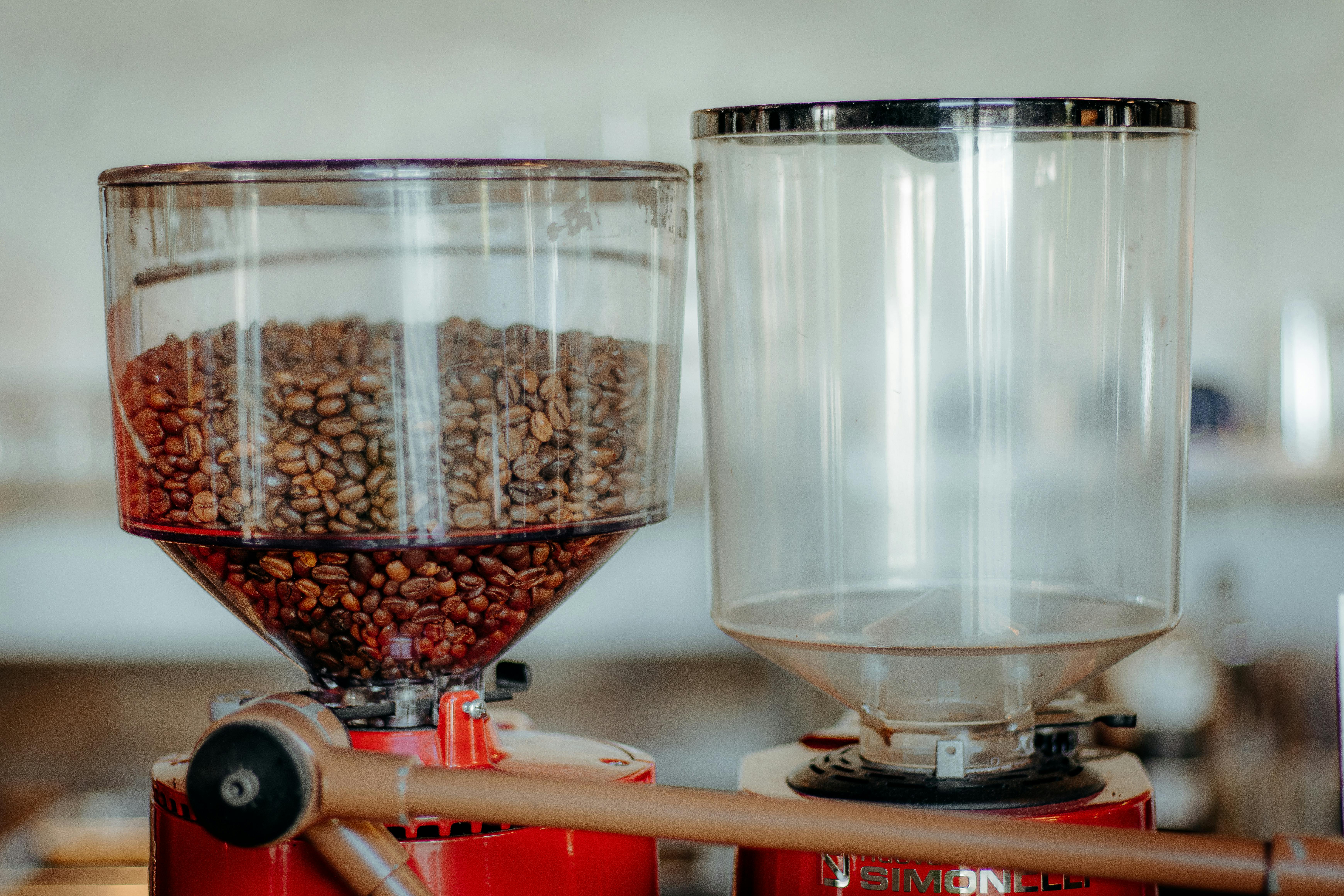 Close-up of a commercial coffee grinder with a full bean hopper in a cafe setting.