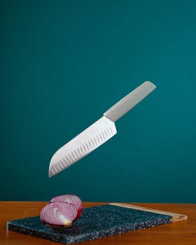 A kitchen knife hovers above a chopping board with a sliced red onion below.