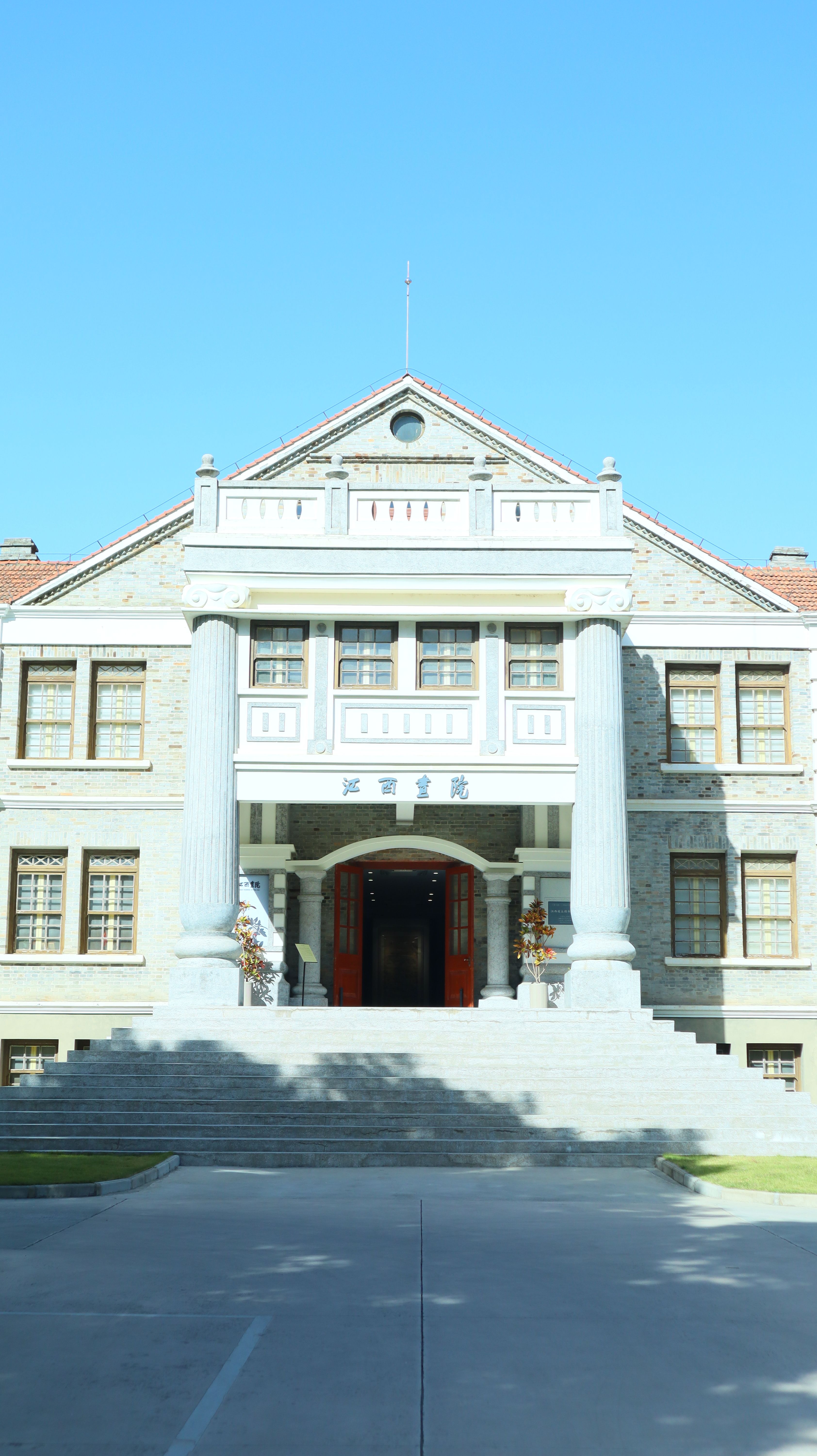 Elegant facade of a historic stone building with large columns and stairs, under a bright blue sky.