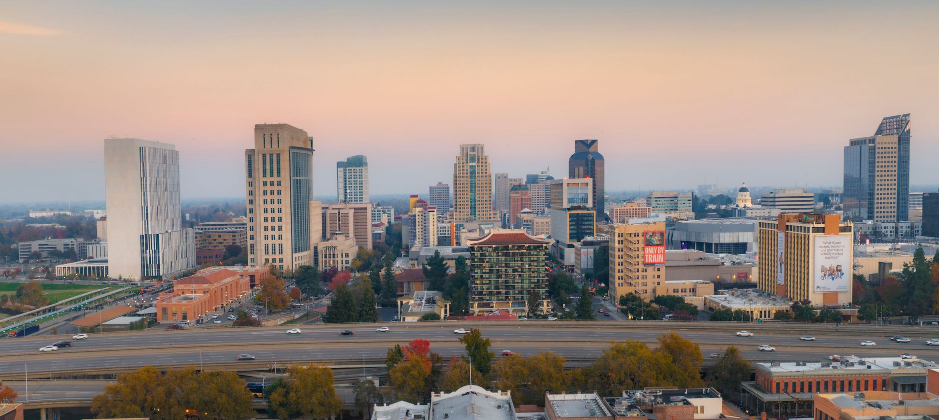 Aerial view of Sacramento skyline at dawn with colorful sky, showcasing tall buildings and vibrant city life.