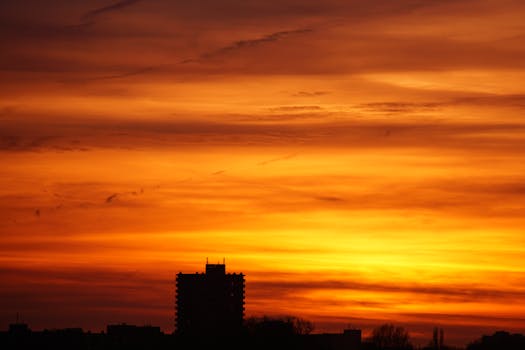 A stunning cityscape silhouette against a vibrant orange sunset with dramatic clouds.