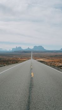 Long scenic road stretching through the Arizona desert with distant rock formations under a cloudy sky.