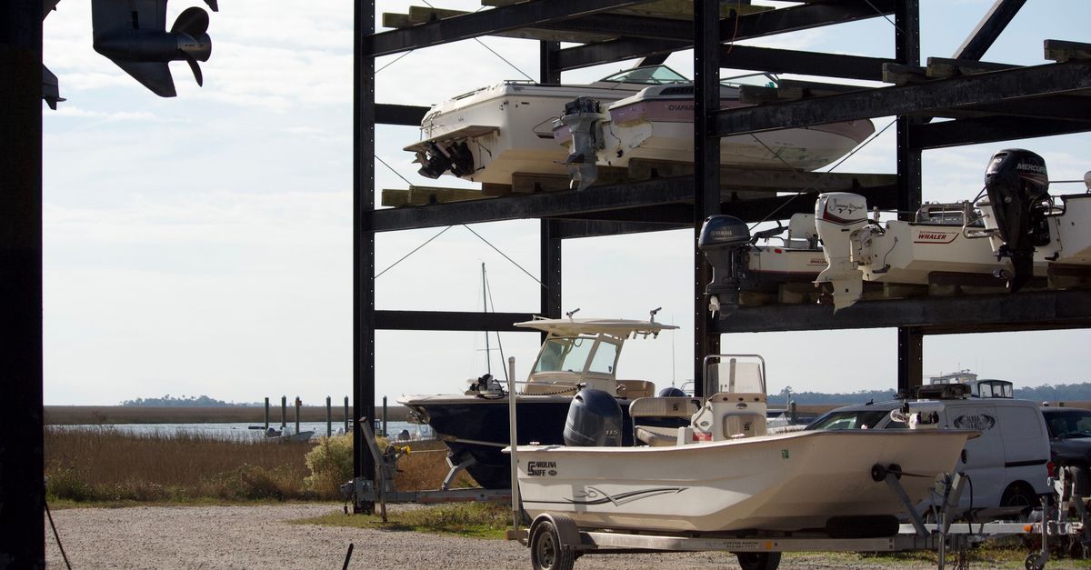 Outdoor marina storage with stacked boats on racks by a waterfront pier.