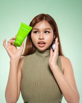 Portrait of a young woman showcasing a skincare routine with green skincare products.