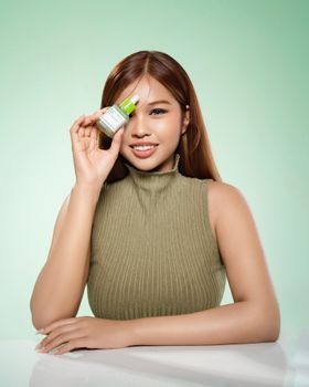 Young woman holding a skincare bottle, showcasing natural beauty in a studio setting.