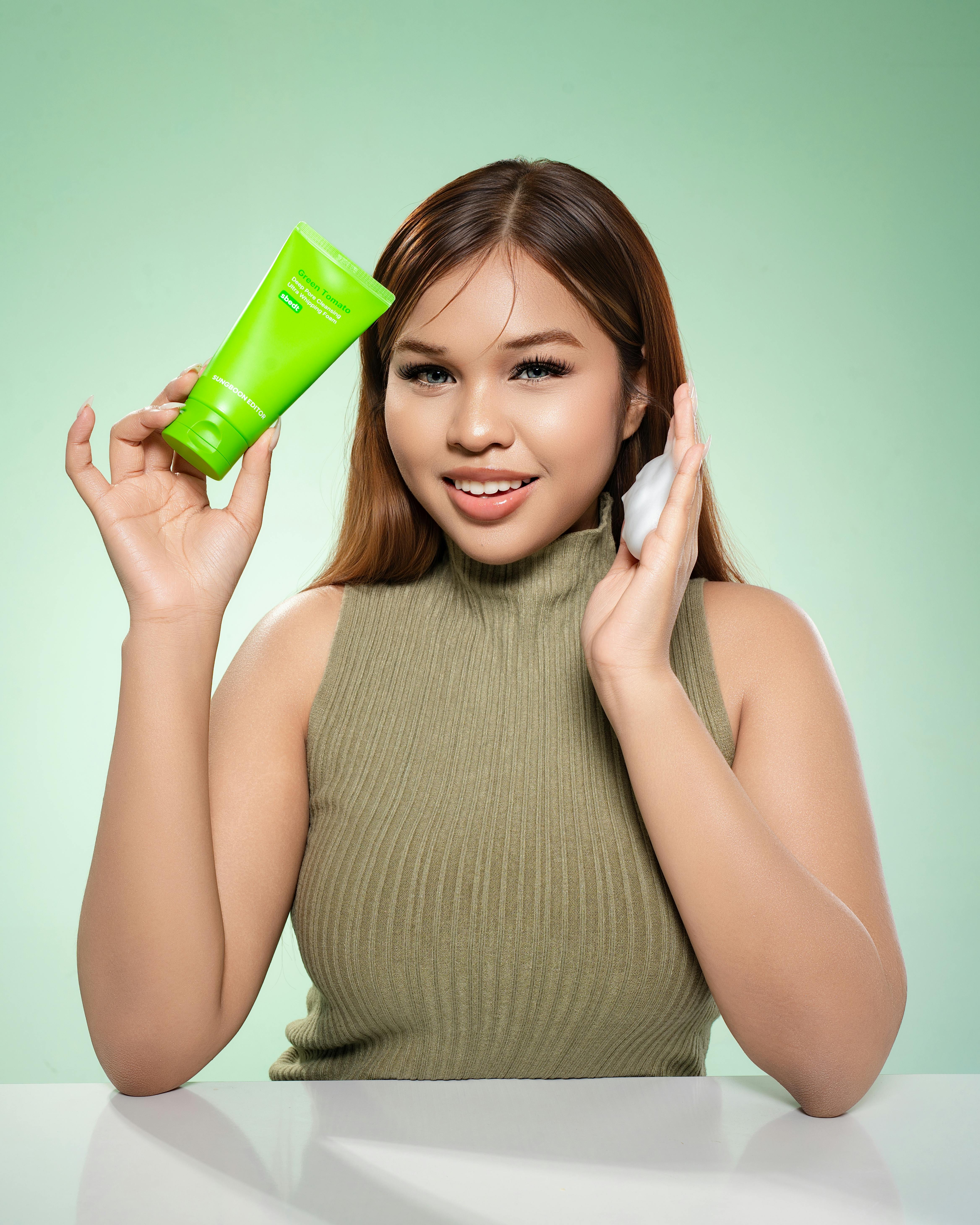 Young woman in Phnom Penh showing skincare routine with a green product, promoting healthy skin.