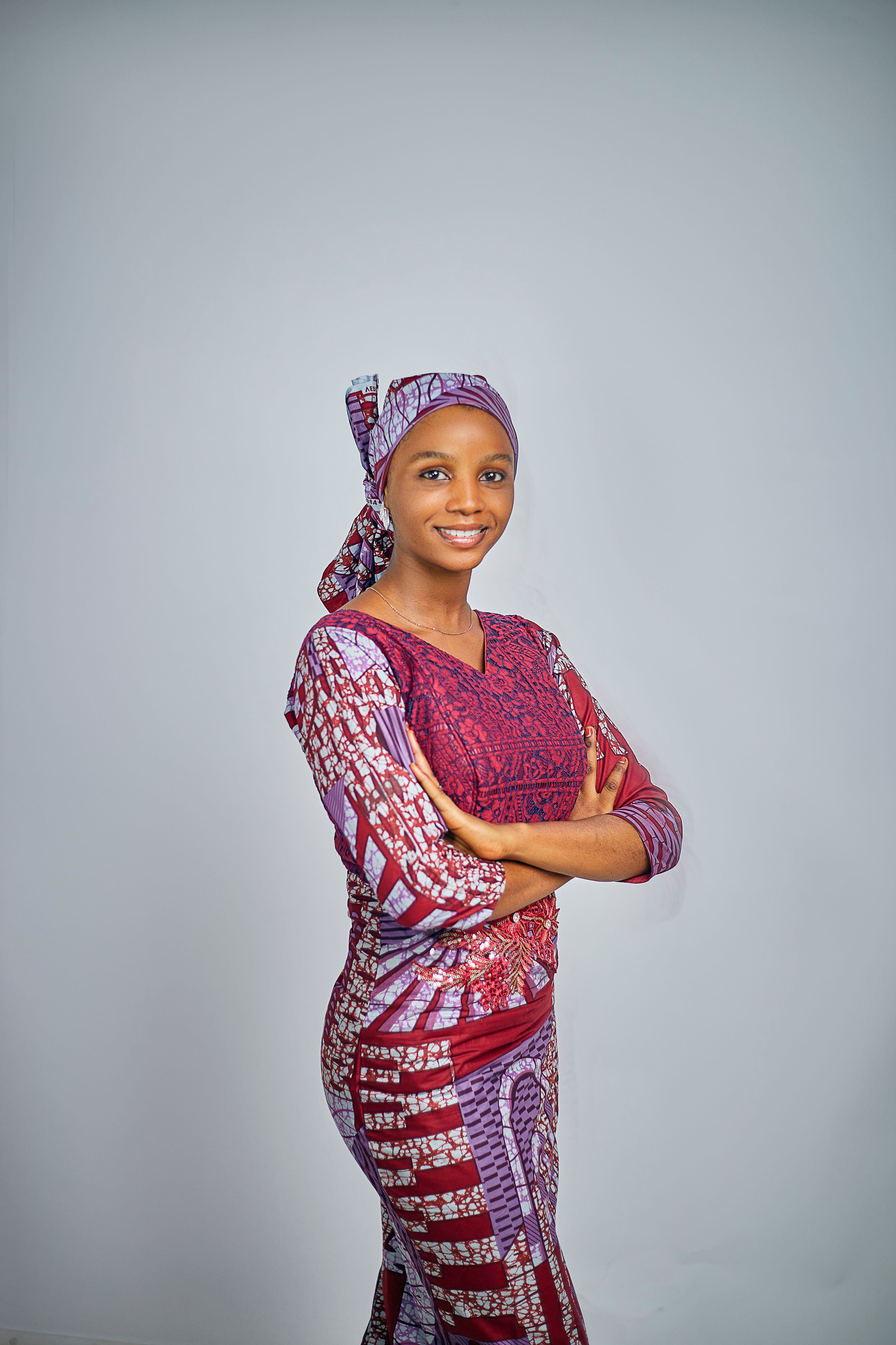 A cheerful woman in colorful traditional dress stands confidently against a neutral backdrop.