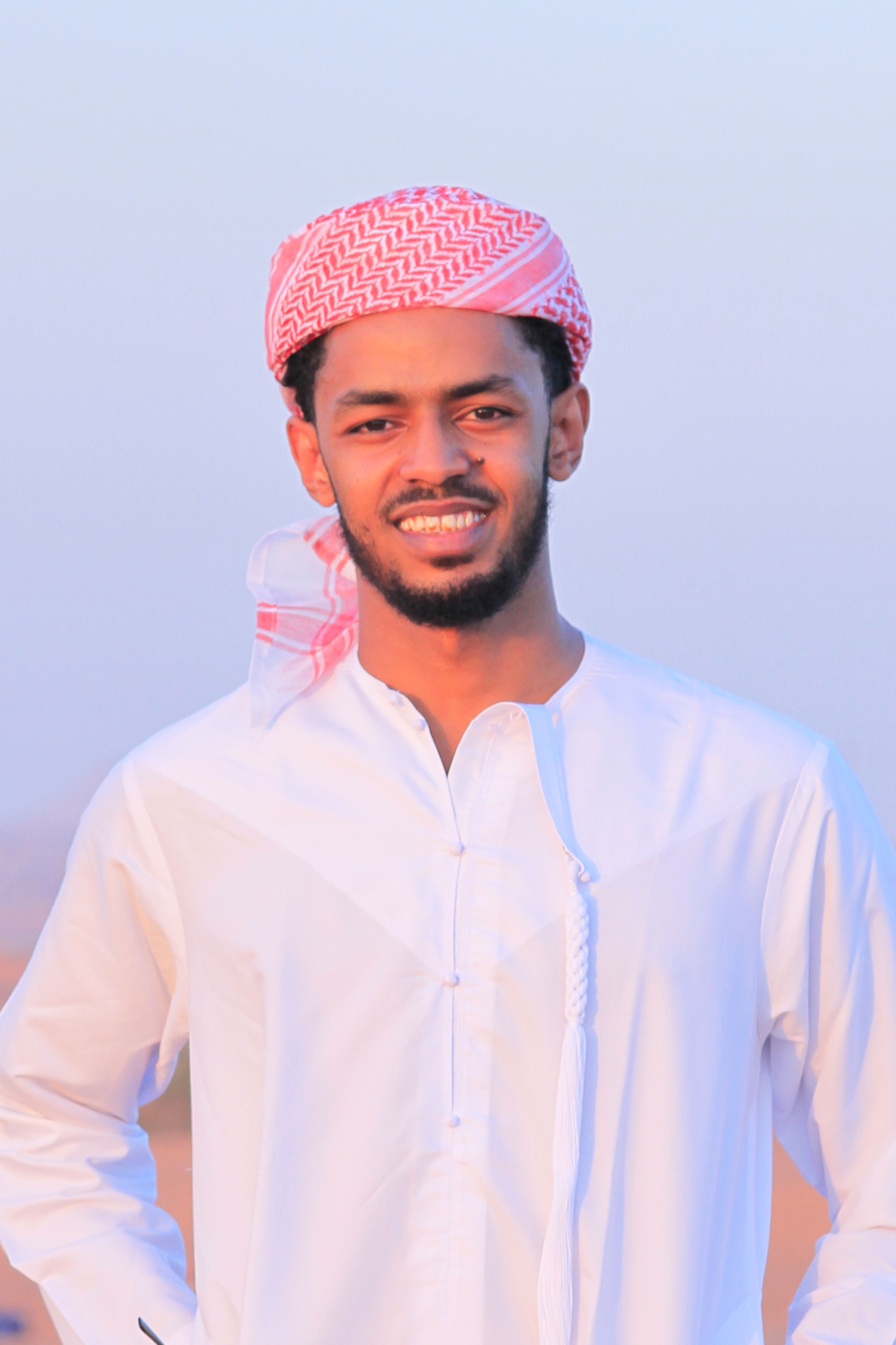 Portrait of a smiling young Middle Eastern man wearing traditional clothing outdoors.