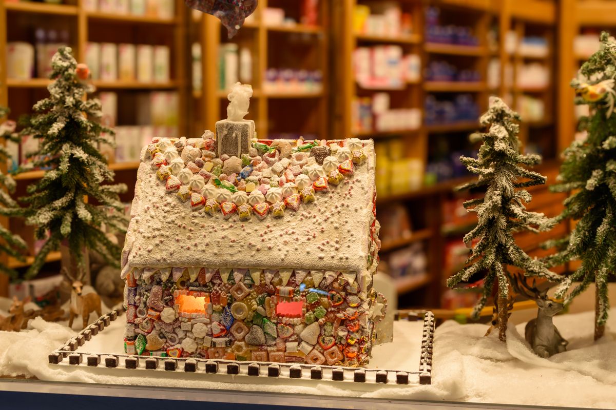 Charming gingerbread house adorned with candy surrounded by snow-dusted trees in a winter wonderland setting.
