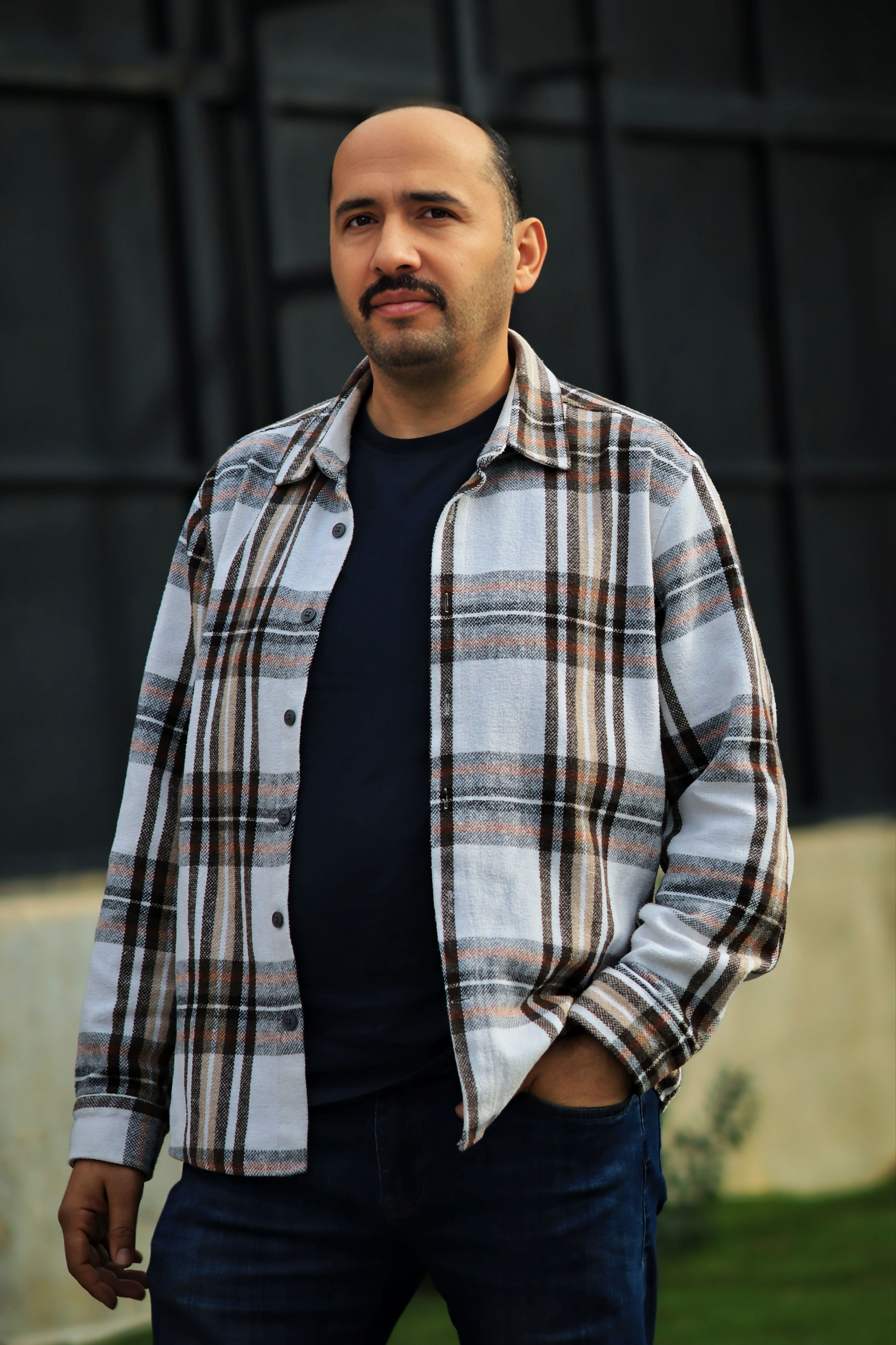 Portrait of a man wearing a plaid shirt standing outdoors.