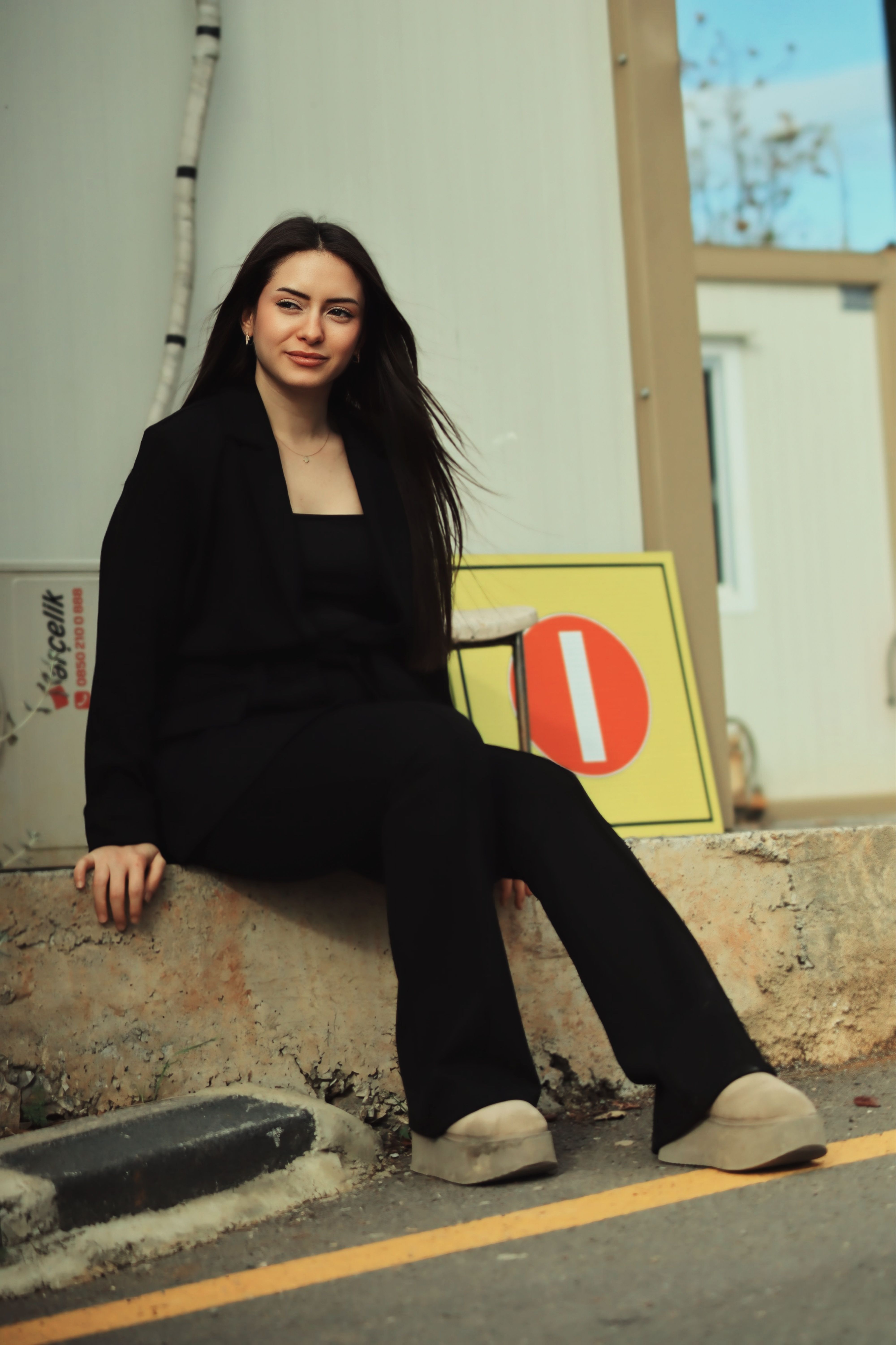 Confident woman in black suit sitting outdoors with relaxed posture.