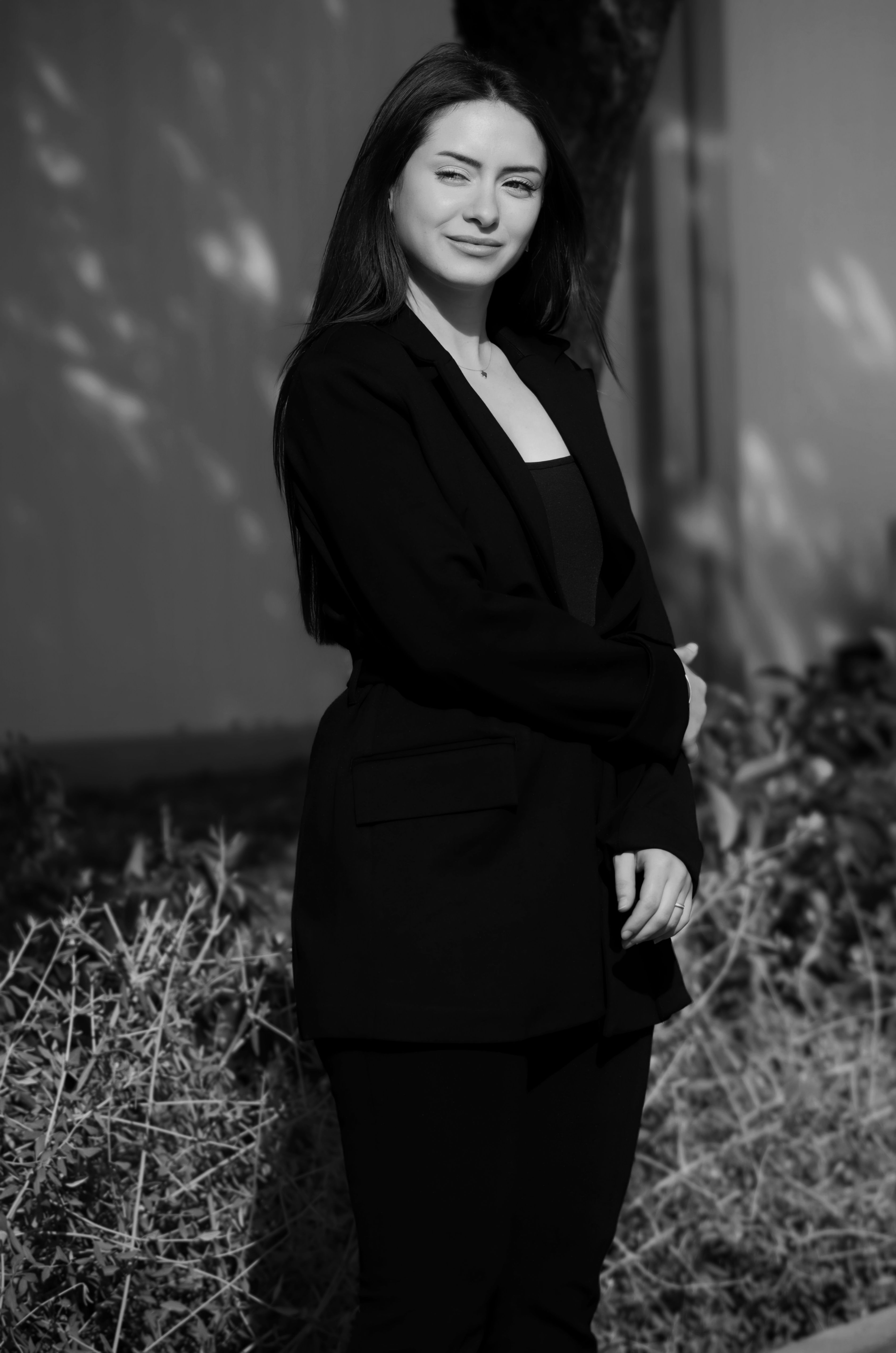 Black and white portrait of a young woman in a black suit standing outside.