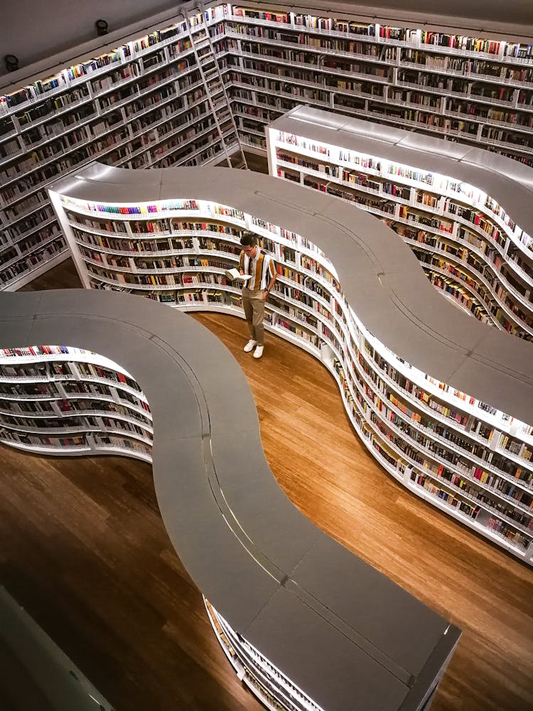 Man Standing Inside Library While Reading Book