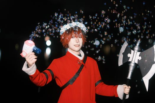 Cosplayer in red outfit holding bubble gun and axe prop at night, surrounded by bubbles.