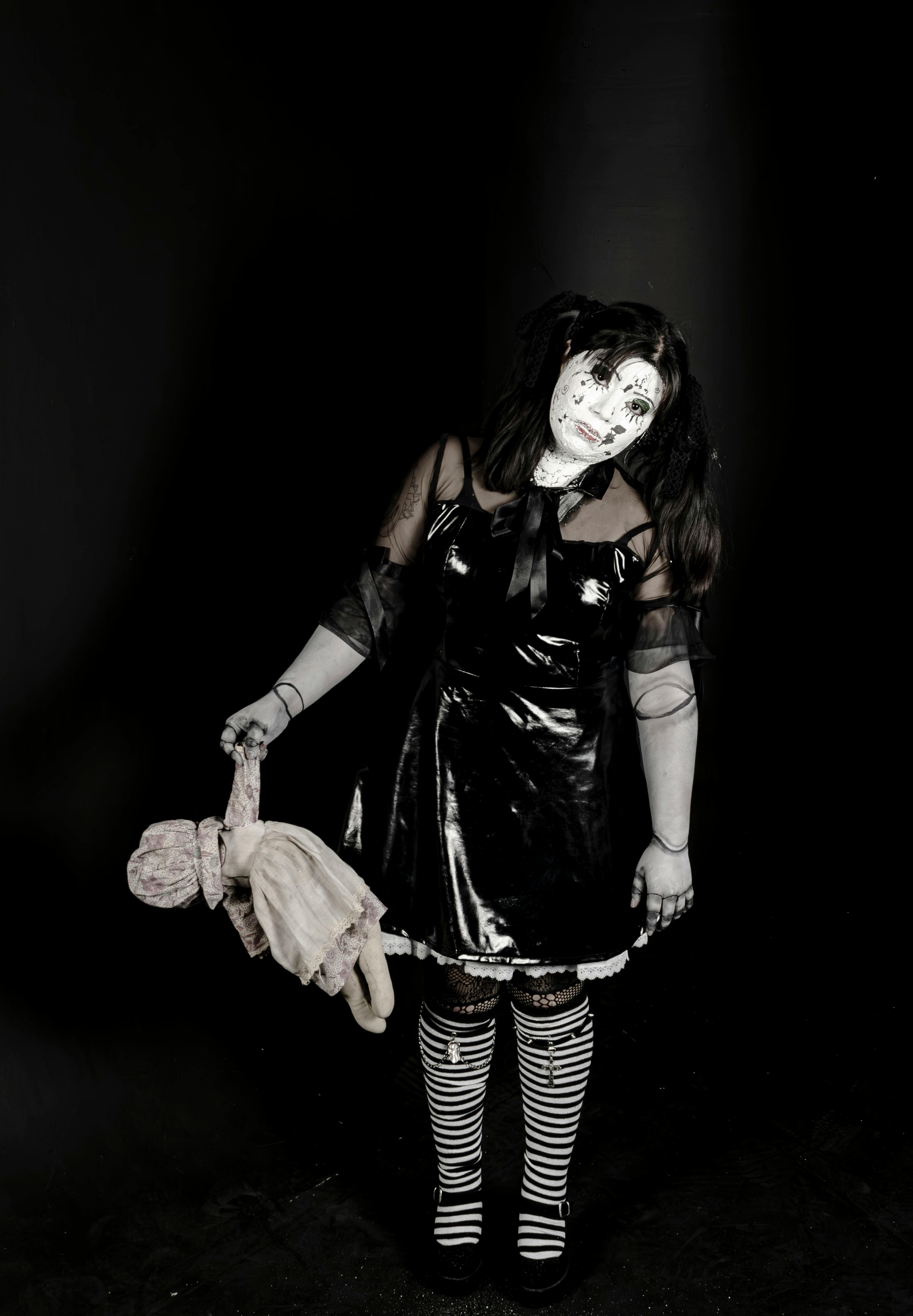 A haunting portrait of a woman in a doll-like costume holding a doll, evoking eerie vibes.
