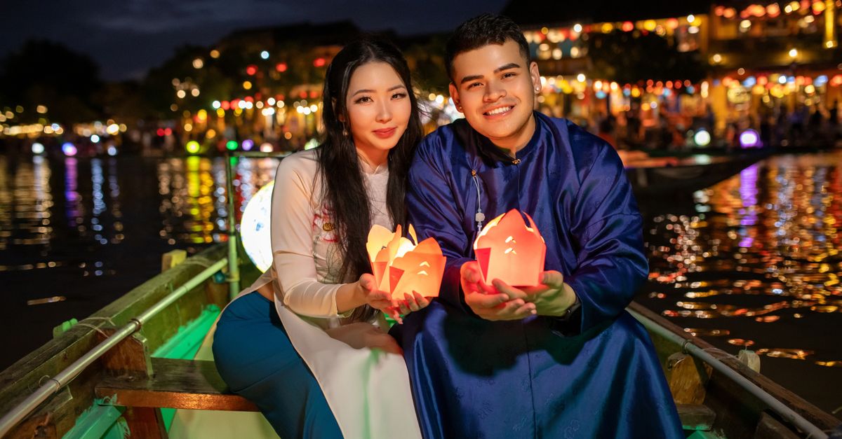 Couple floating candle lanterns on a boat in Hội An, Vietnam, during a vibrant festival night.