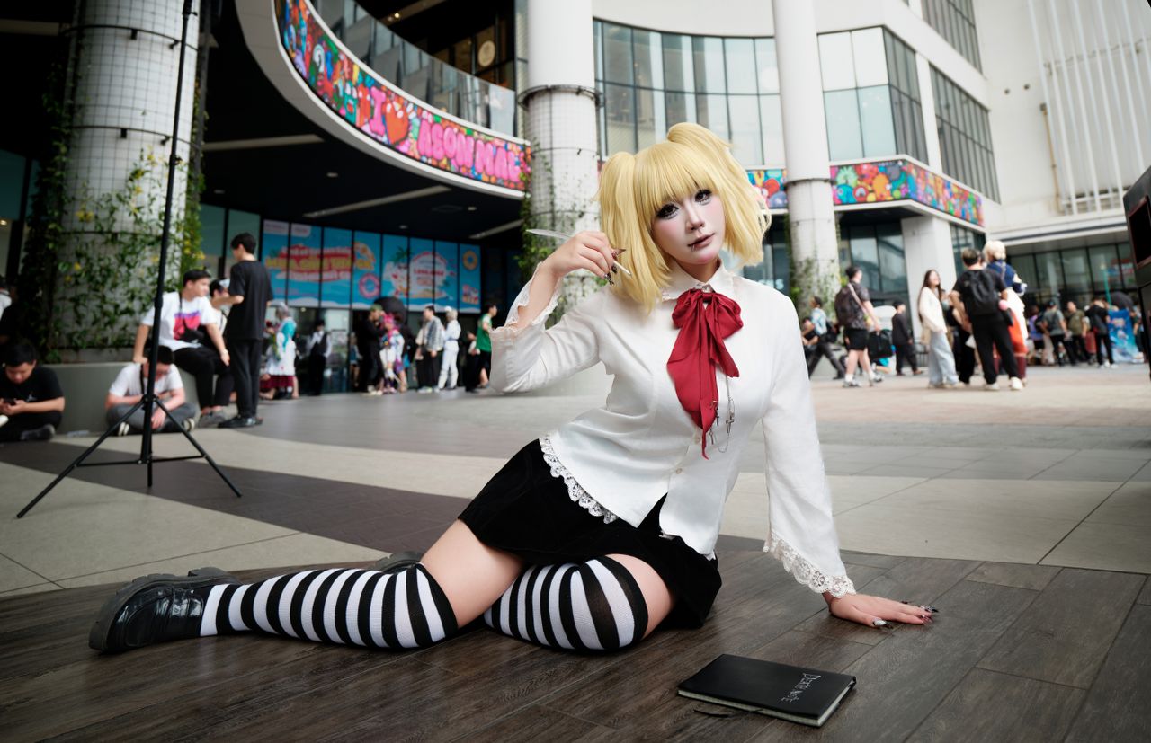 cosplayer in stylish outfit sits at outdoor event surrounded by crowd