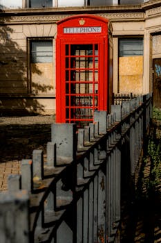 A vibrant red phone booth in an urban scene with moody shadows and historic charm.