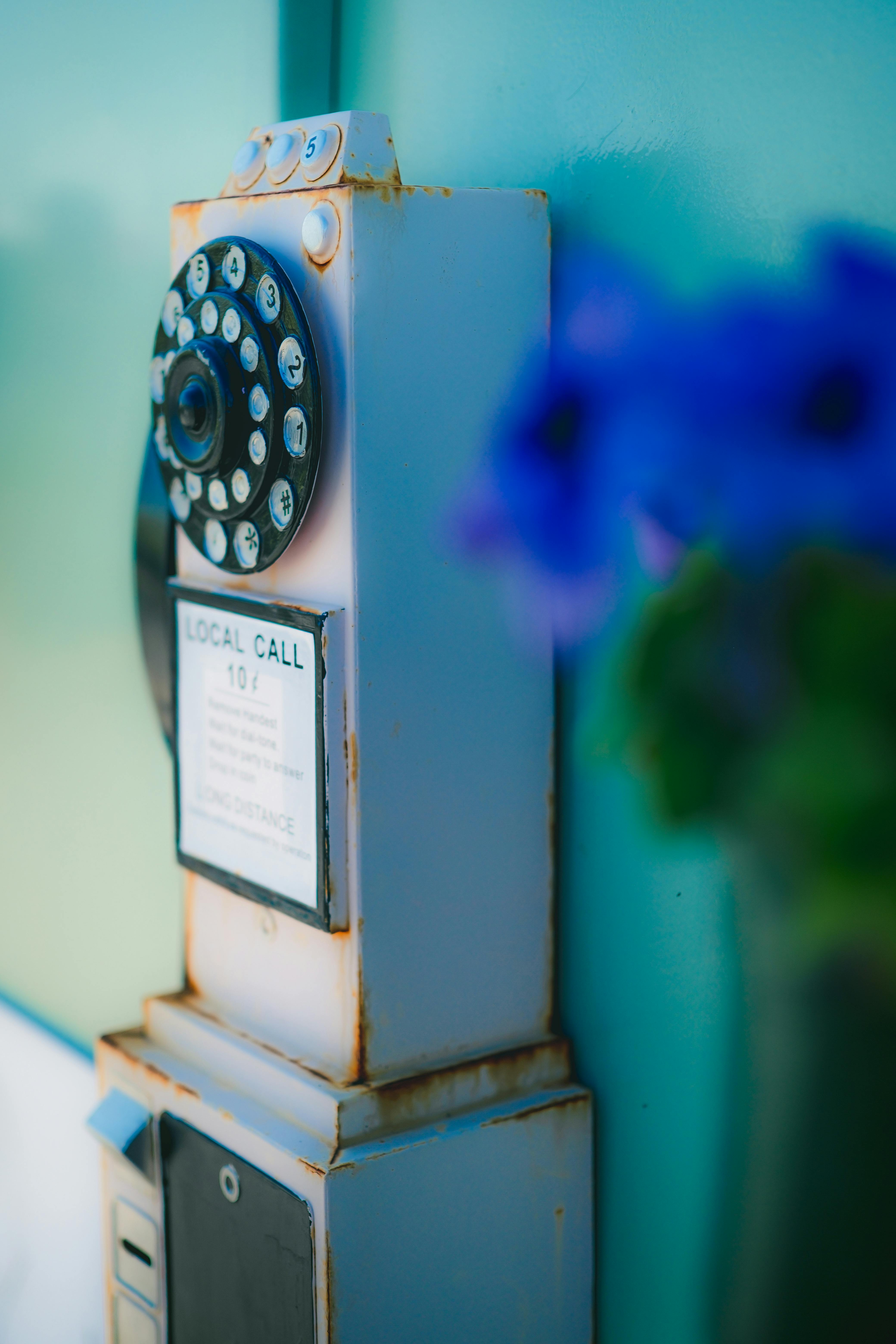 Kostenlos Nahaufnahme einer altmodischen Wählscheibentelefonzelle mit rustikalem Charme und verschwommenen Blumen im Vordergrund. Stock-Foto