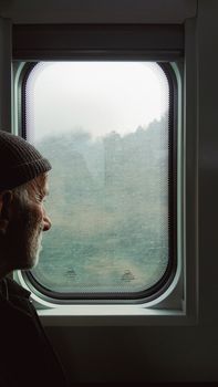 A senior man reflects while looking out a train window during a journey.