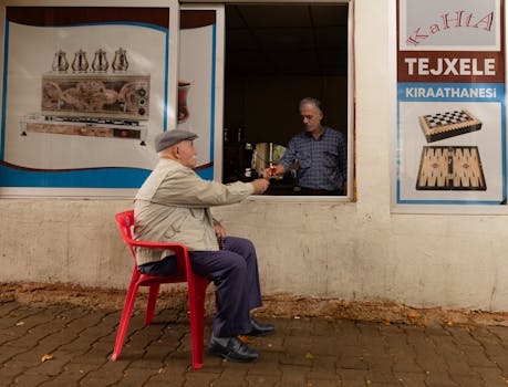 Two elderly men exchange a cup of tea through a café window, a scene of daily life.