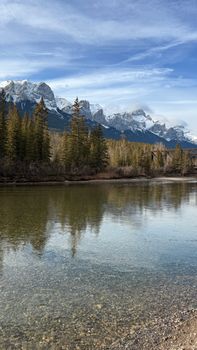 Serene landscape of the Rocky Mountains reflected in a clear river with pine trees.