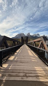 A picturesque bridge extends towards snow-capped mountains under a vibrant sky.