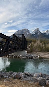 Steel rail bridge crossing river with majestic snow-capped mountains in the background.