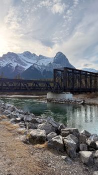 Majestic snow-covered peaks rise above a serene railway bridge over a tranquil river.