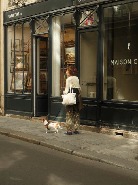A woman walking her dog past a Parisian gallery, capturing the essence of city life.