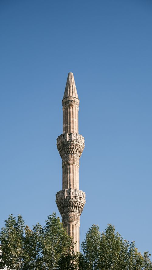 Free Elegant minaret tower against a clear blue sky framed by green trees. Stock Photo