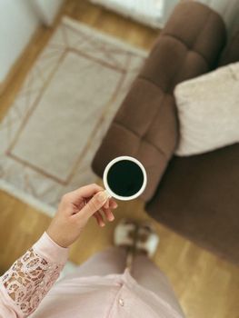 Bird's eye view of person holding coffee in cozy home setting, highlighting relaxed lifestyle.
