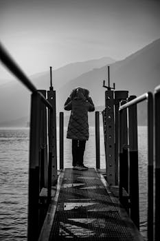 A person stands alone on a pier overlooking a serene lake, evoking solitude and introspection.
