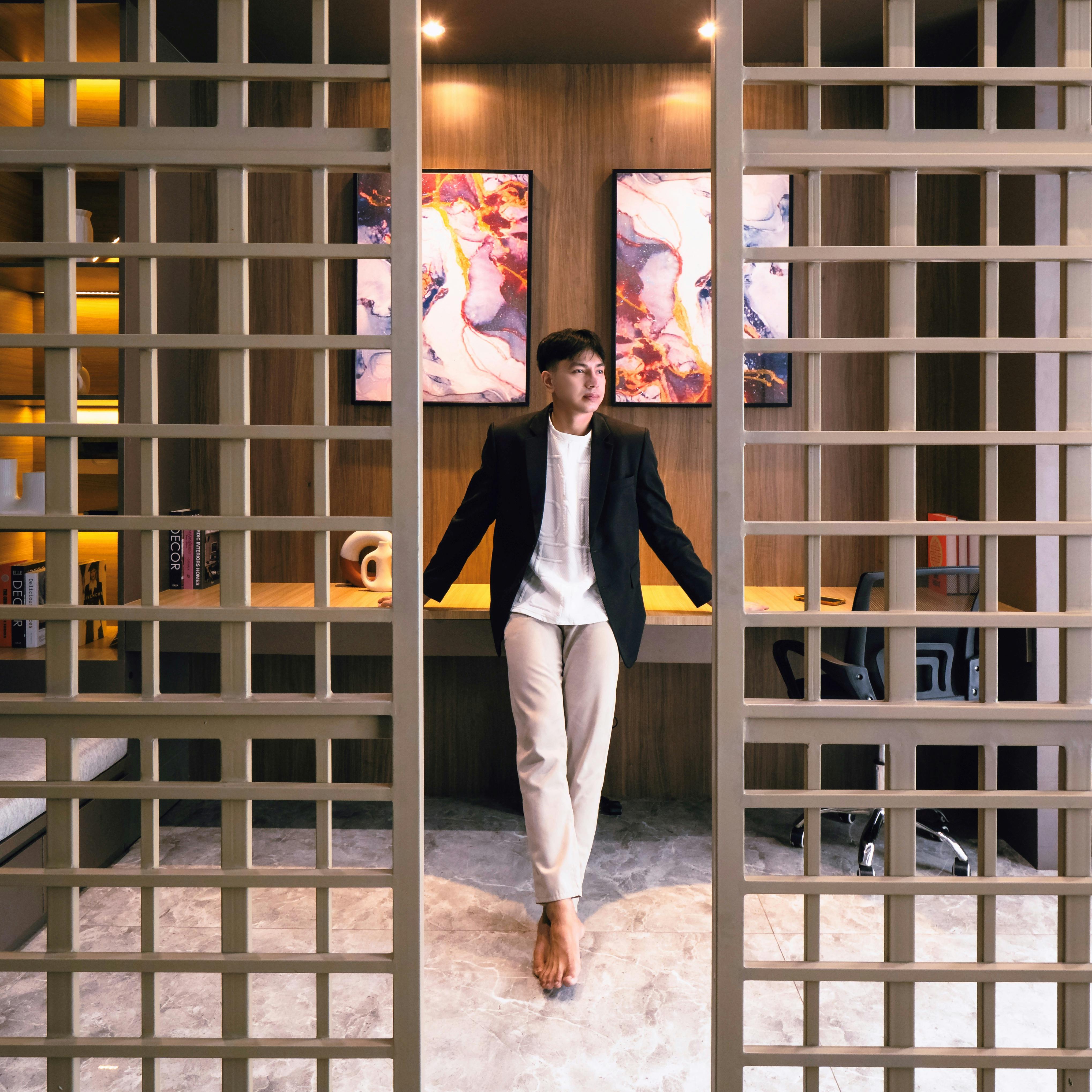 A young adult leans against a stylish partition in a contemporary home office with art decor.