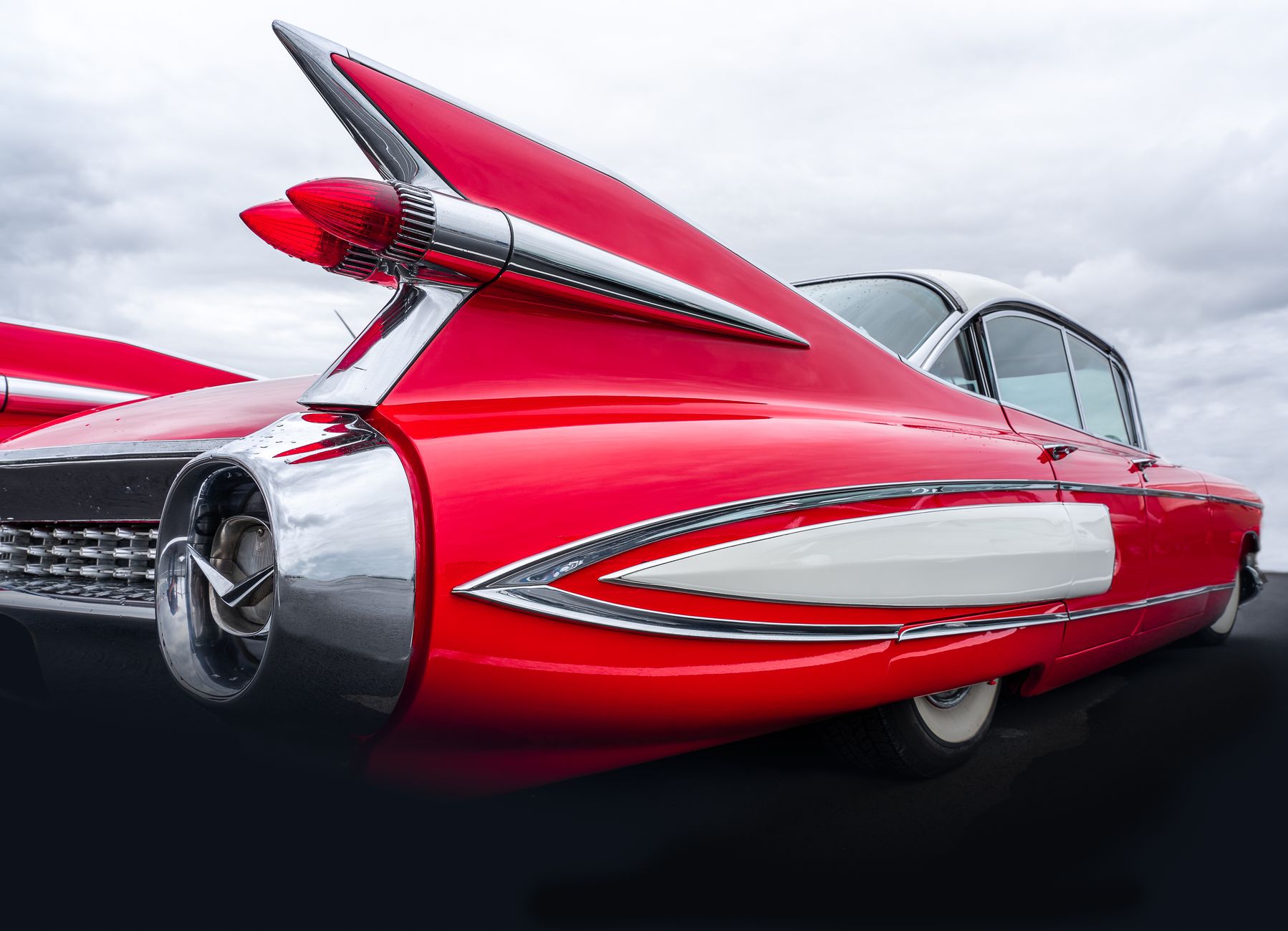 Close-up view of a retro red Cadillac showcasing its iconic tail fins and chrome details under a cloudy sky.