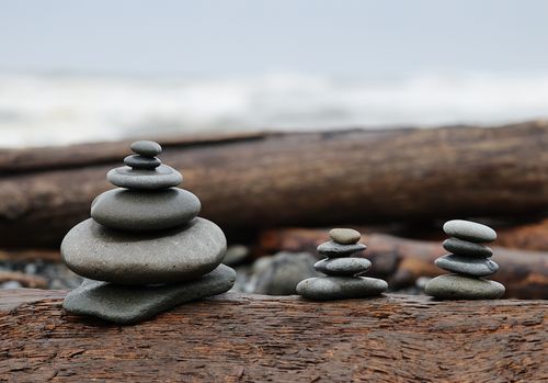 Free Balanced pebble cairns on weathered driftwood at a serene seaside, evoking tranquility and balance. Stock Photo