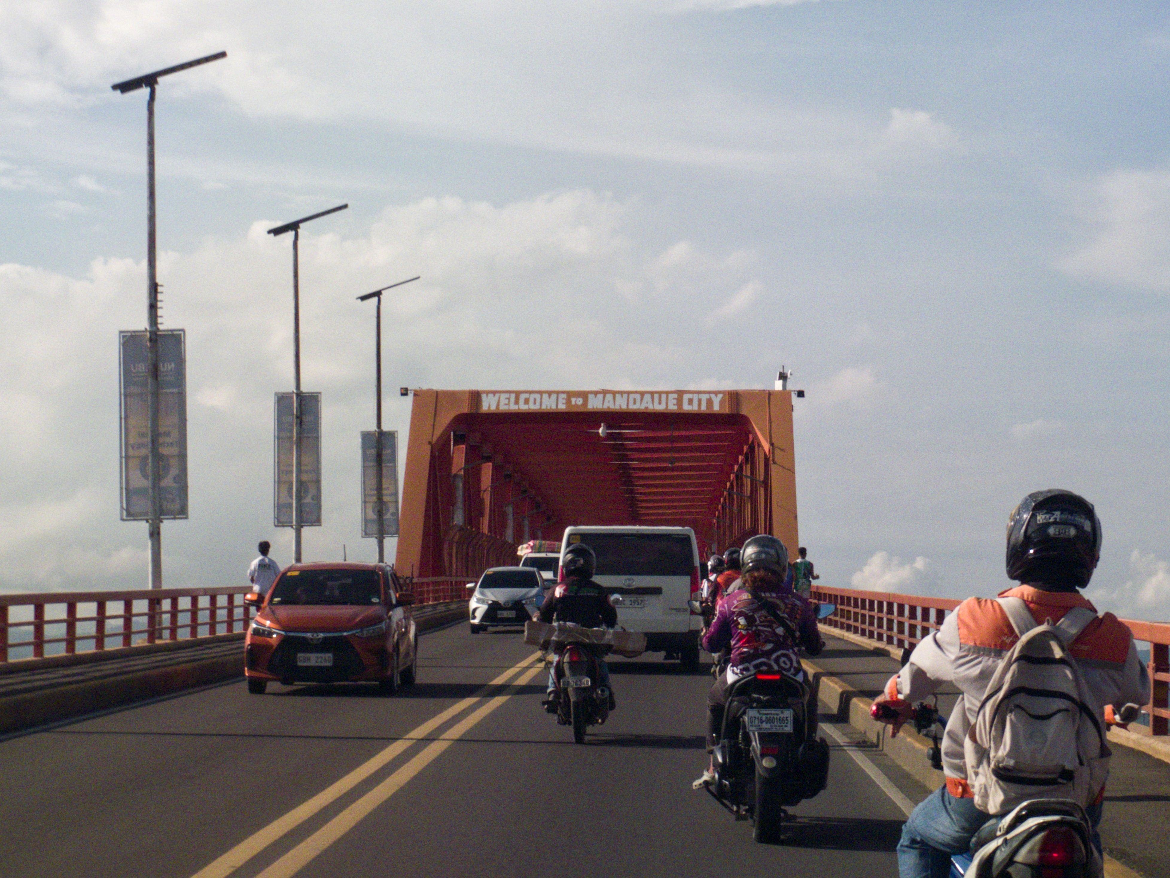 Vehicles crossing a bridge into Mandaue City, with clear blue skies overhead.