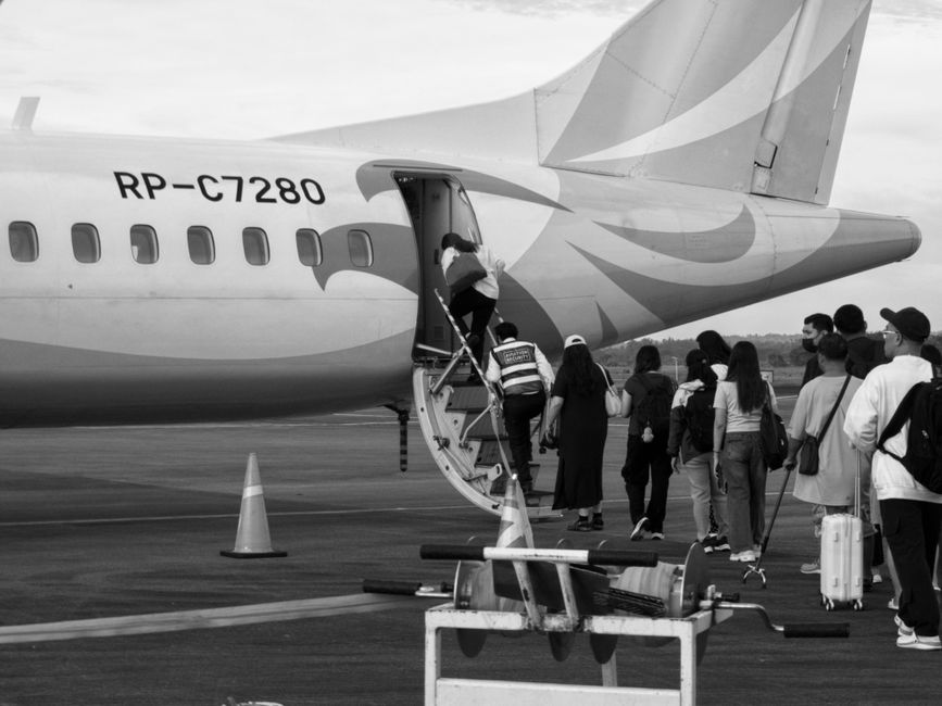 Black and white photo of people boarding a small propeller airplane on the tarmac.