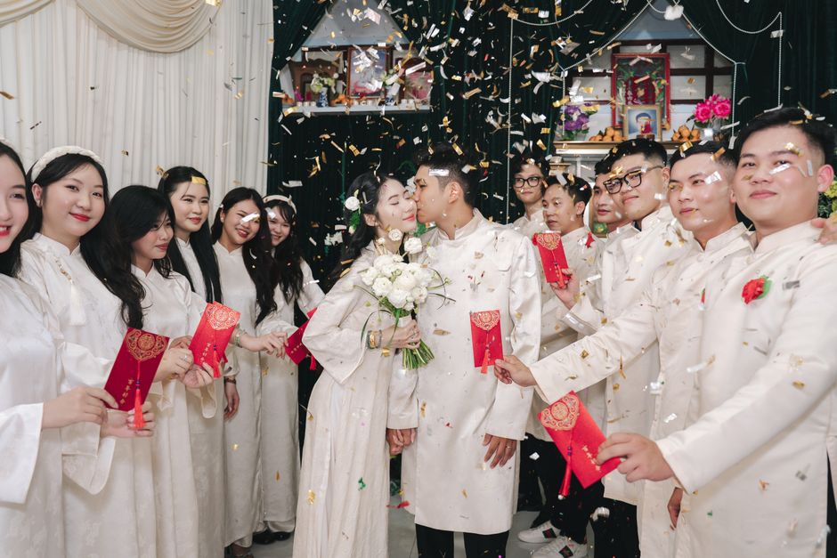 Bride and groom kiss amid festive wedding celebration with traditional attire and confetti.