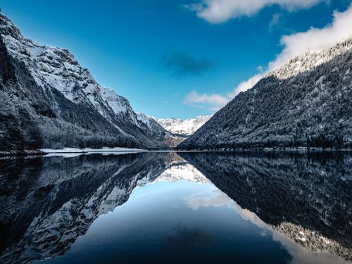 Free Tranquil view of snow-covered mountains reflected in a clear lake in Glarus, Switzerland. Stock Photo