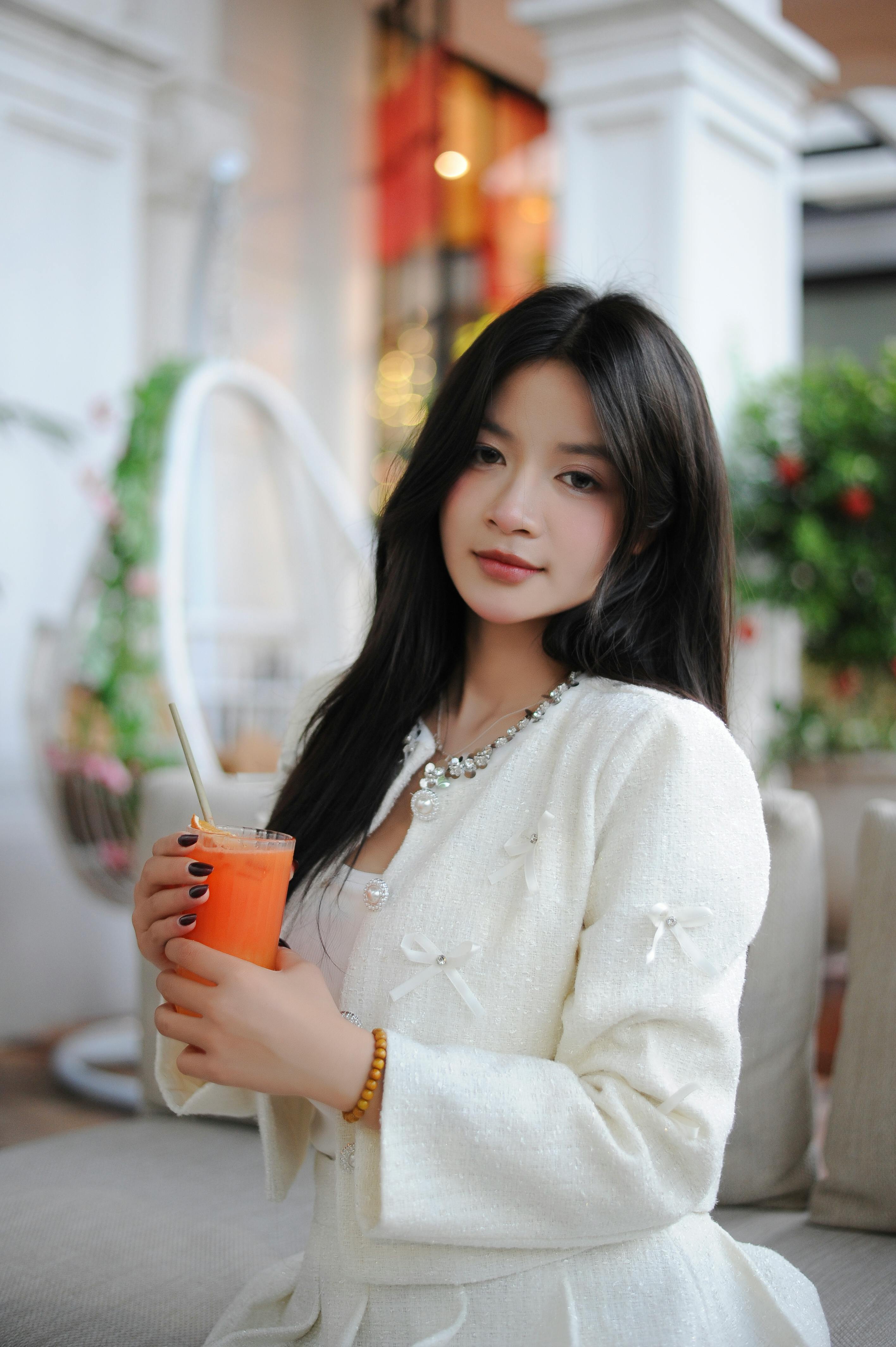 Chic woman in white attire enjoys a refreshing carrot juice inside a modern cafe.
