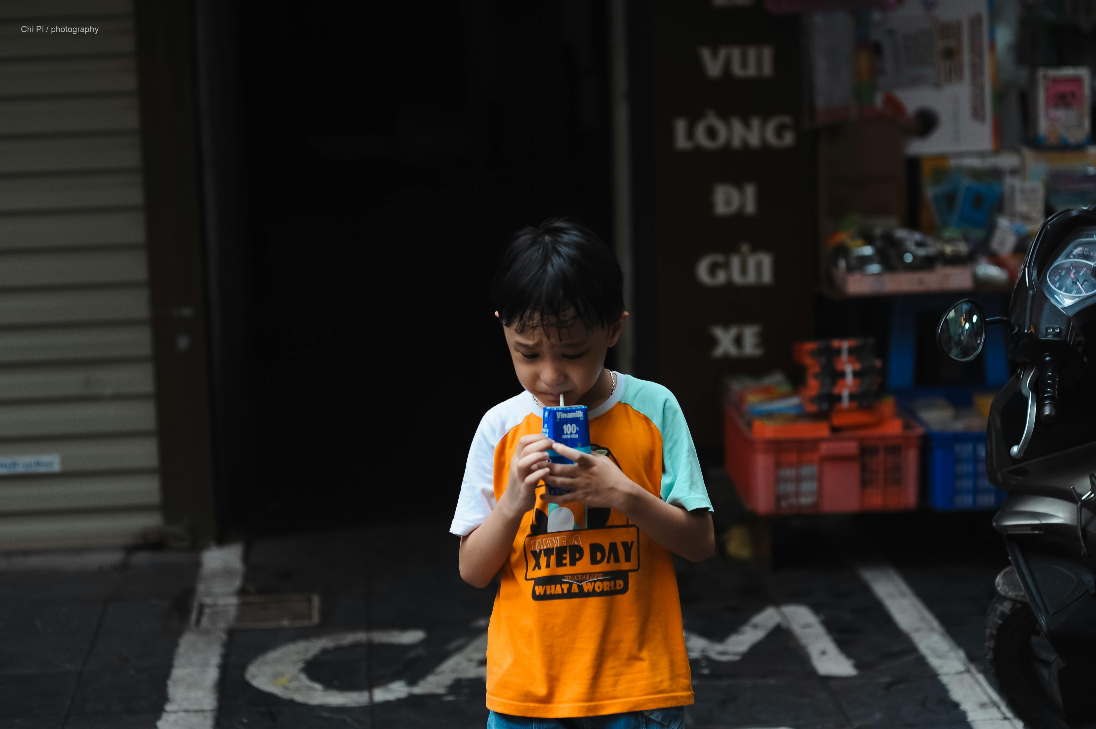Free A young boy enjoys a juice box on a city street, captured in a candid moment. Stock Photo