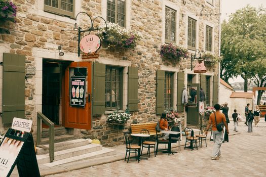 A picturesque view of a stone building with flower pots in Old Québec City, bustling with people.