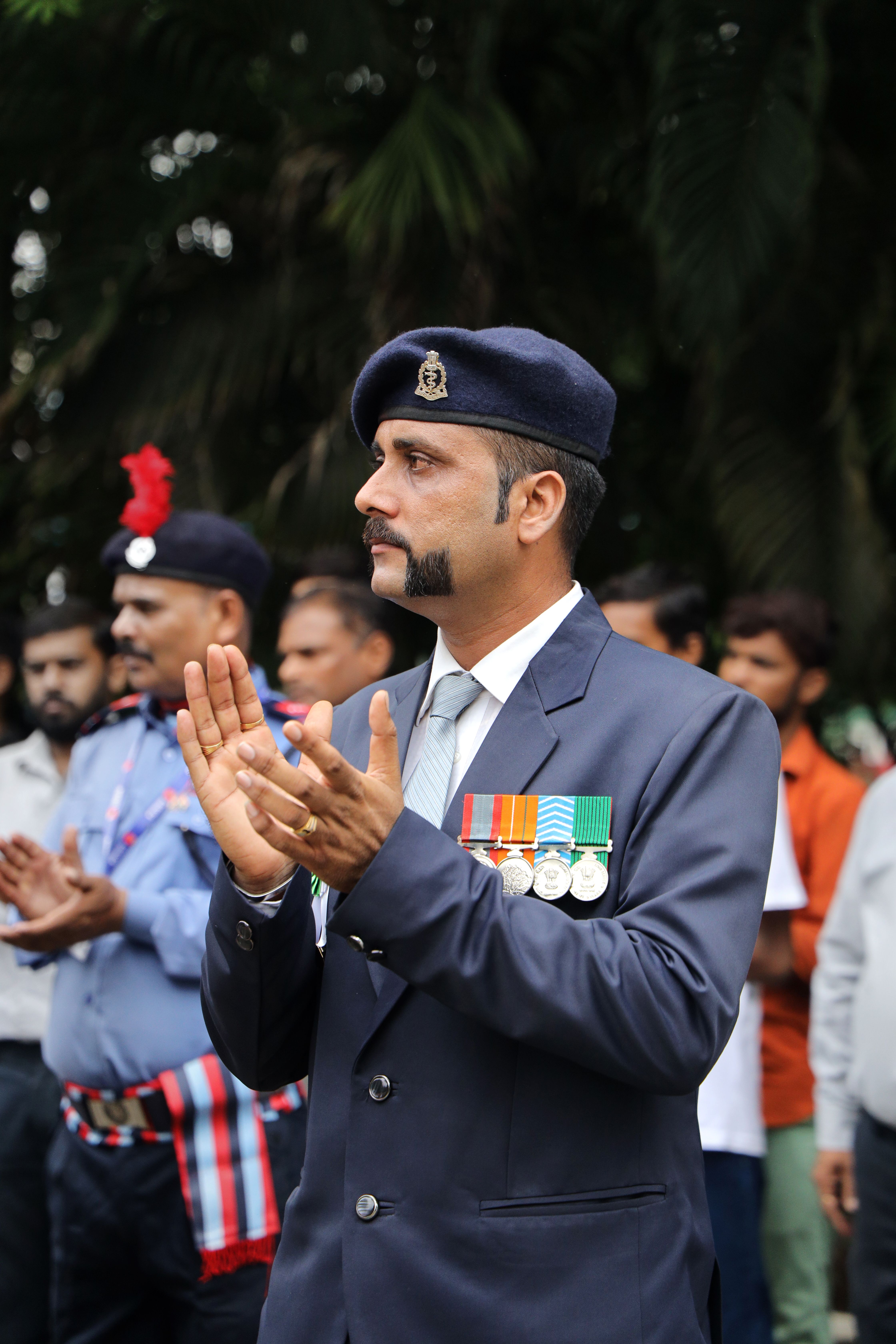 Indian military officer clapping during an outdoor event, surrounded by colleagues.