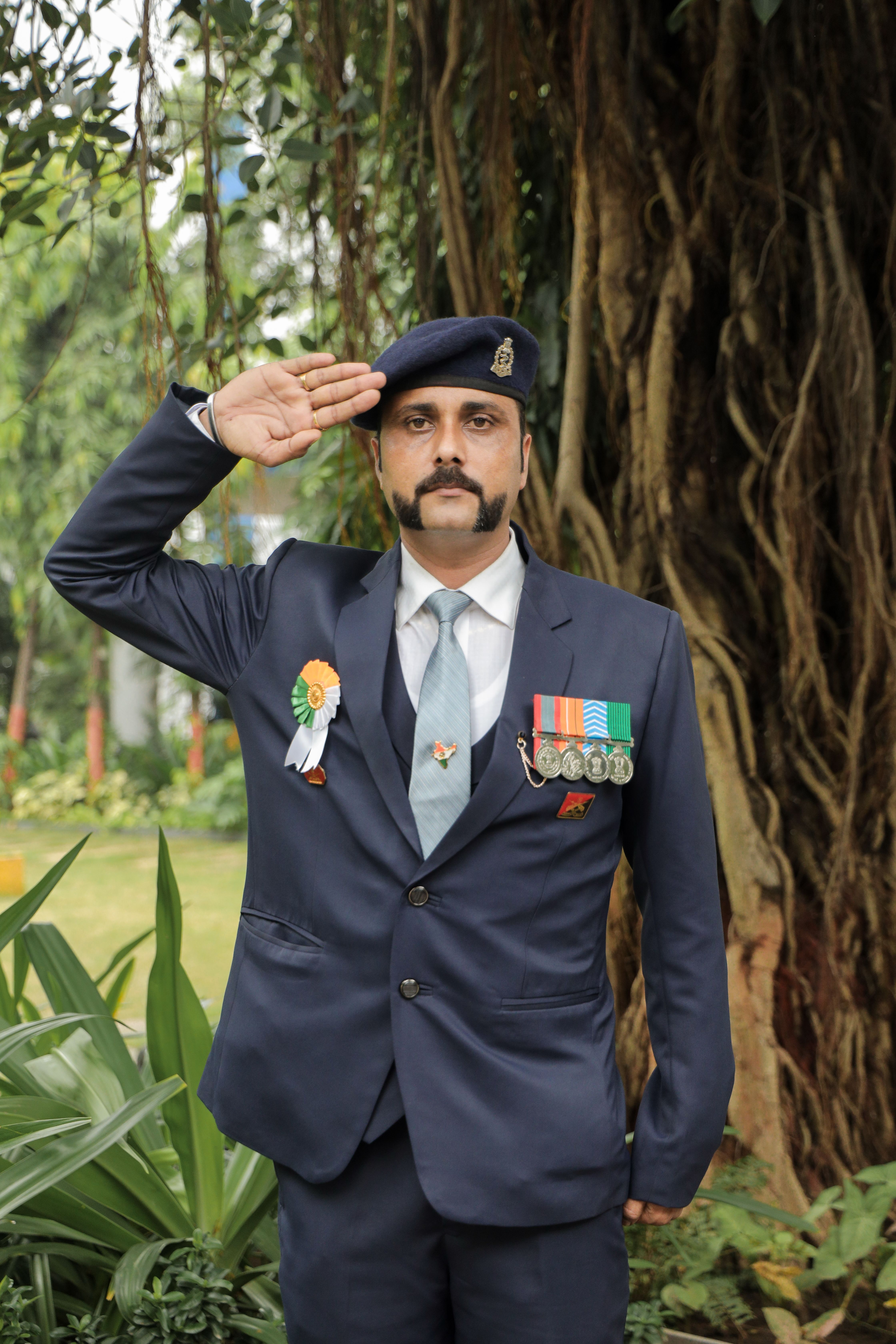South Asian military officer in formal attire saluting, outdoors background.